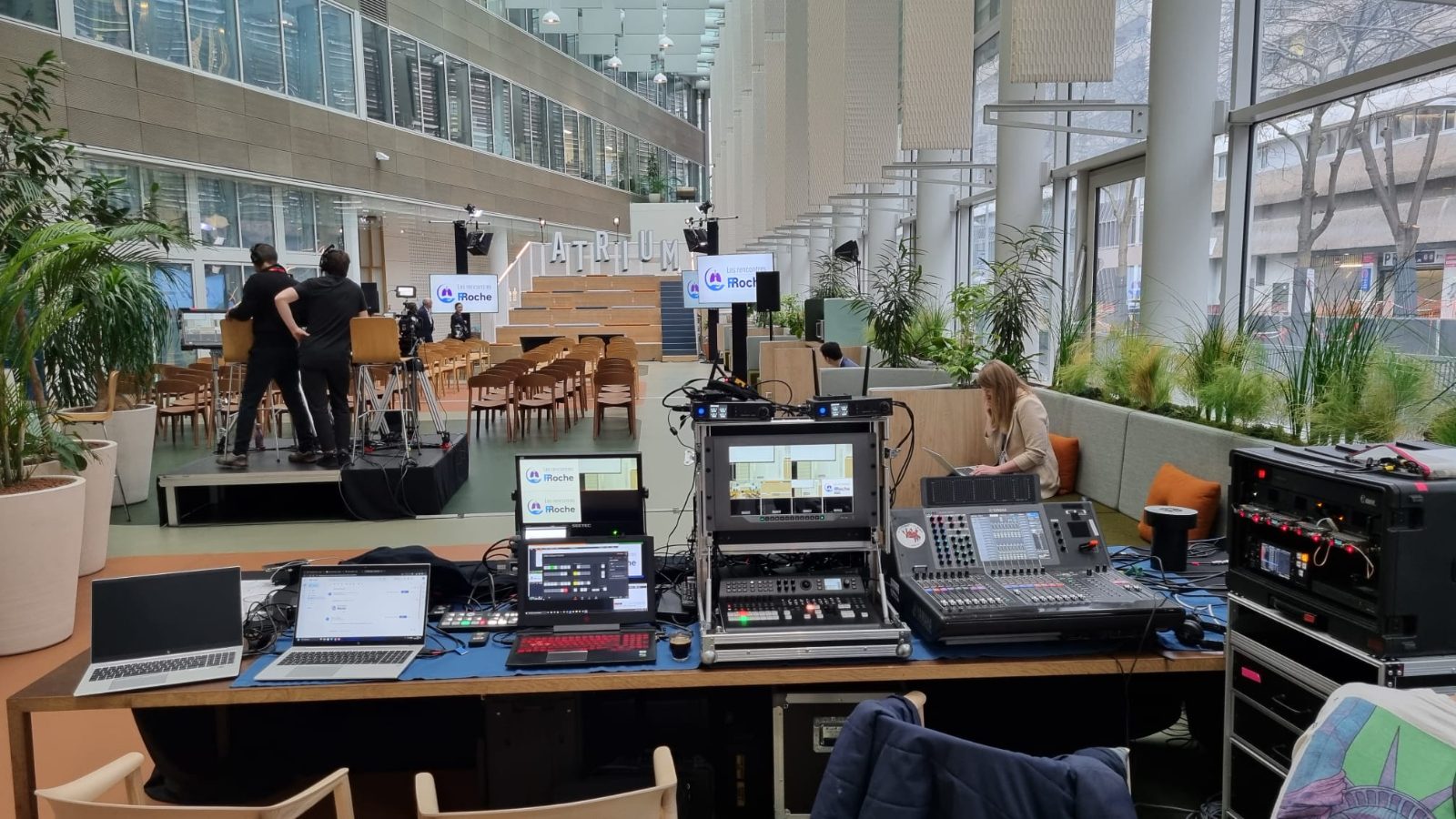 Sound and video control set up in an atrium, mixing console, house screens and the set beyond
